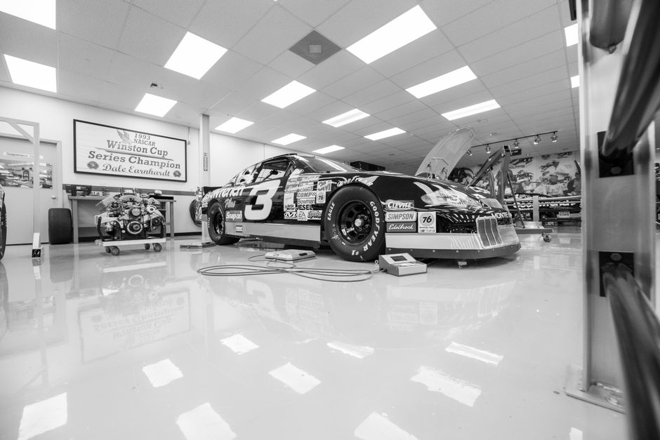 Black and white photo of a classic race car in a workshop with a vintage sign.